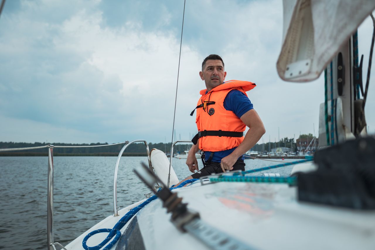 cursos A man in a life vest sailing on a lake, showcasing adventure and safety.