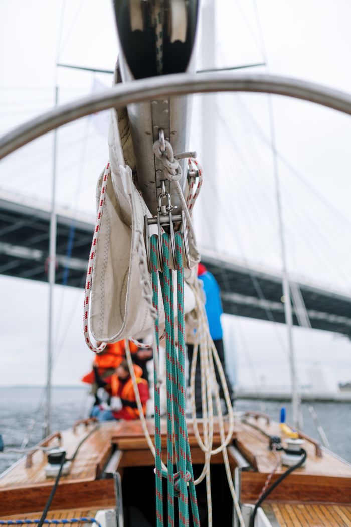 Close-up of a sailboat mast and ropes, capturing the essence of a sailing journey beneath a bridge.